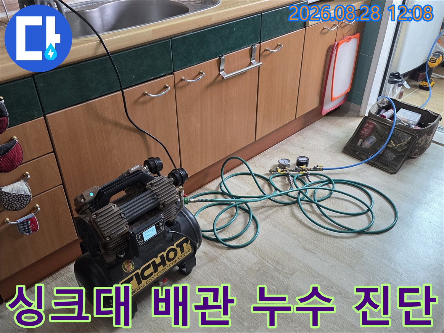 싱크대 하부장 아래에 놓인 공압 장비와 연결된 배관 점검 모습입니다.