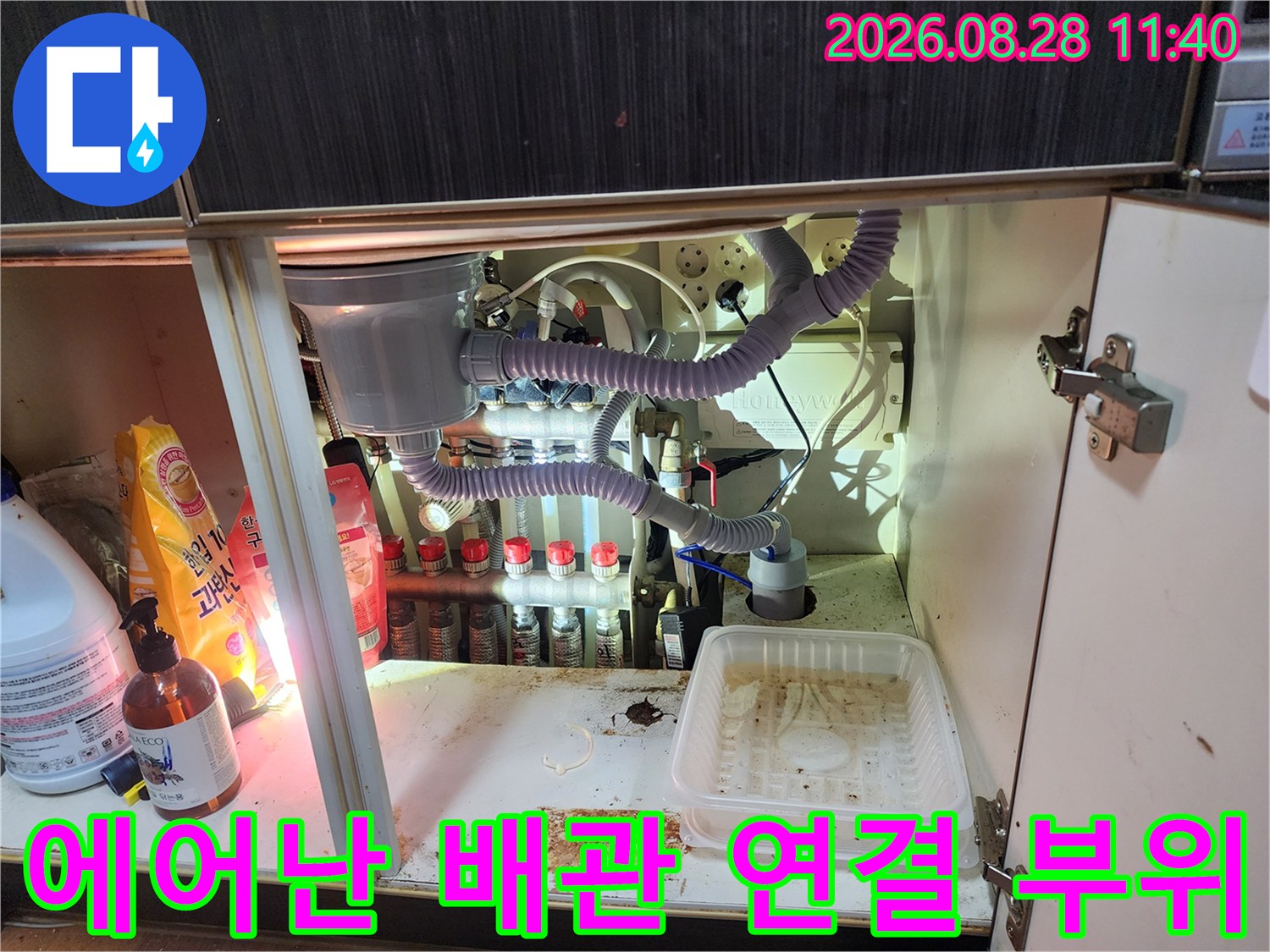 에어컨 드레인 호스와 정수기 라인이 복잡하게 얽힌 싱크대 하부장 내부 사진