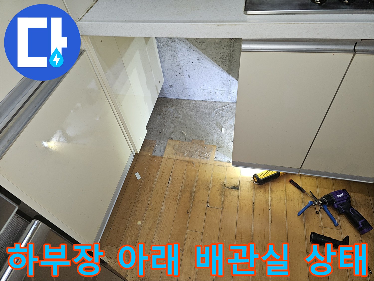 싱크대 하단 공간에 드러난 배관 통로와 작업 도구들