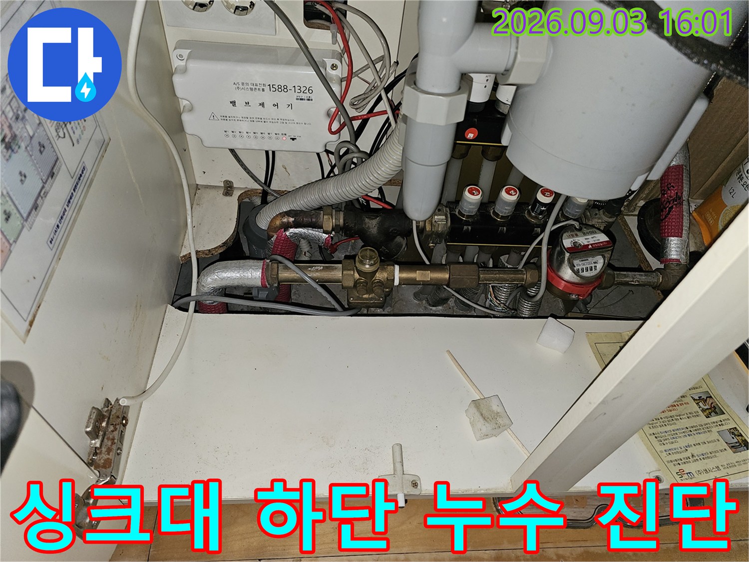 싱크대 하부의 보일러 배관과 분배기 부속품들의 연결 상태를 정밀하게 점검하는 장면입니다.
