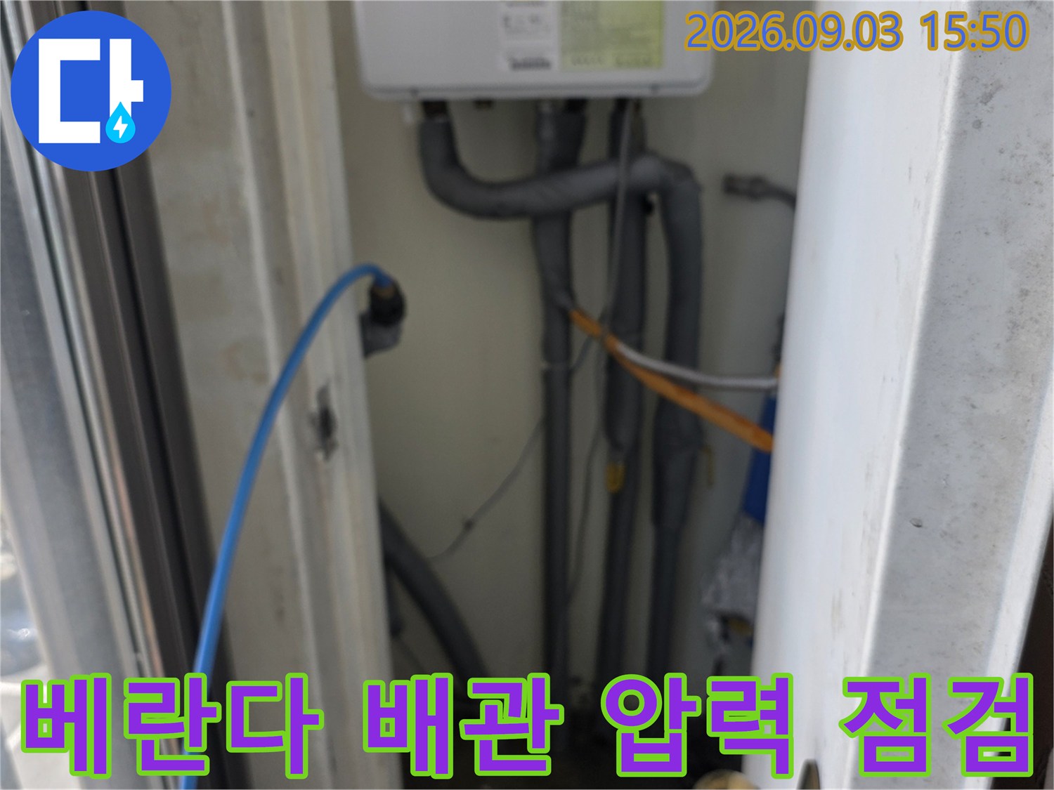 하얀색 계량기함 근처의 배관들에 연결된 검사용 호스와 장비입니다.