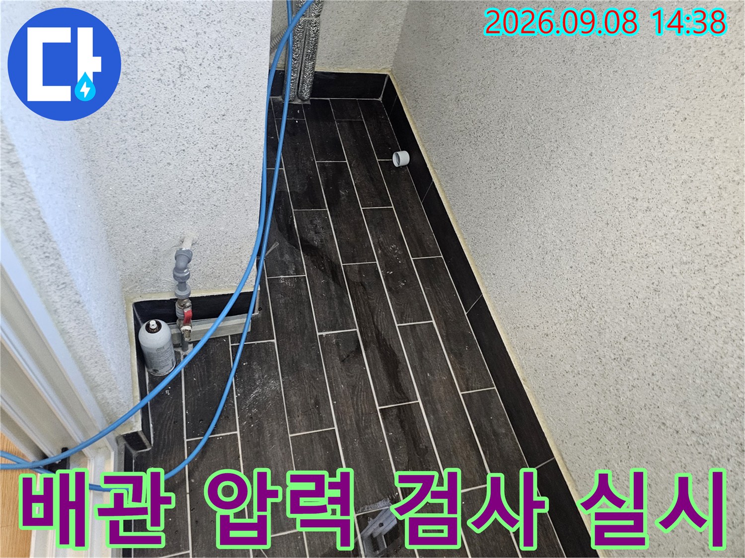 파란색 에어 호스가 연결된 타일 벽면의 배관 점검 장치