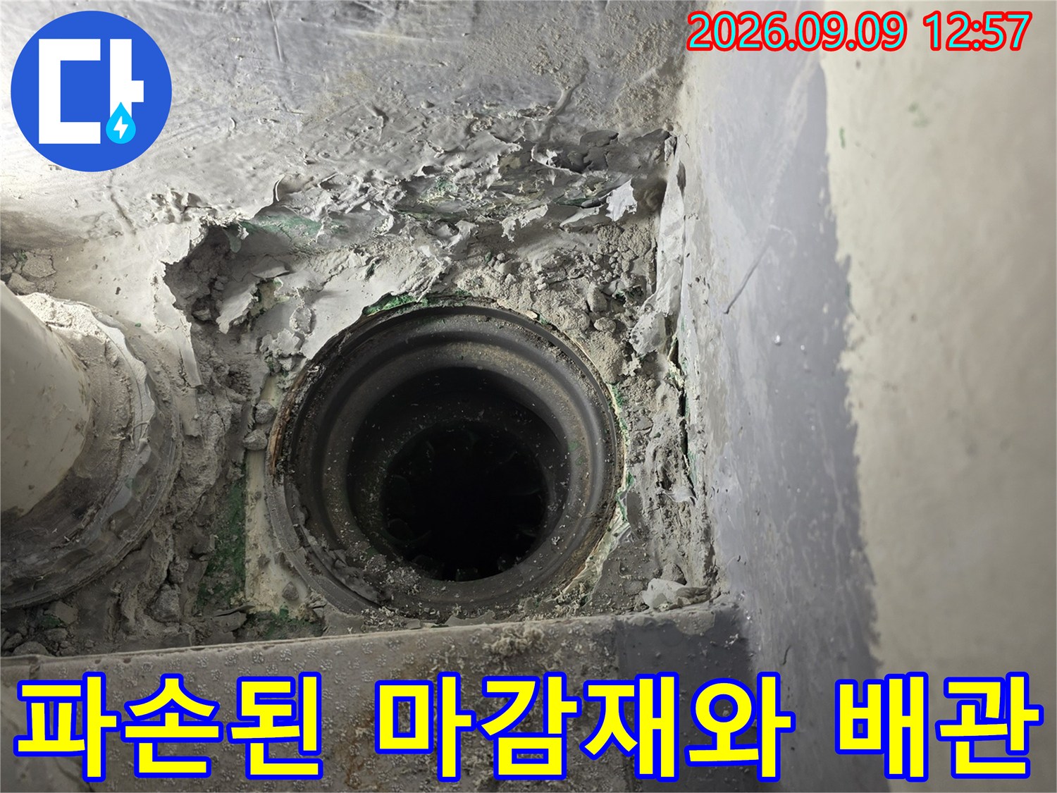 배수관 주변의-부서진 시멘트와 노출된 배관 연결 부위입니다.