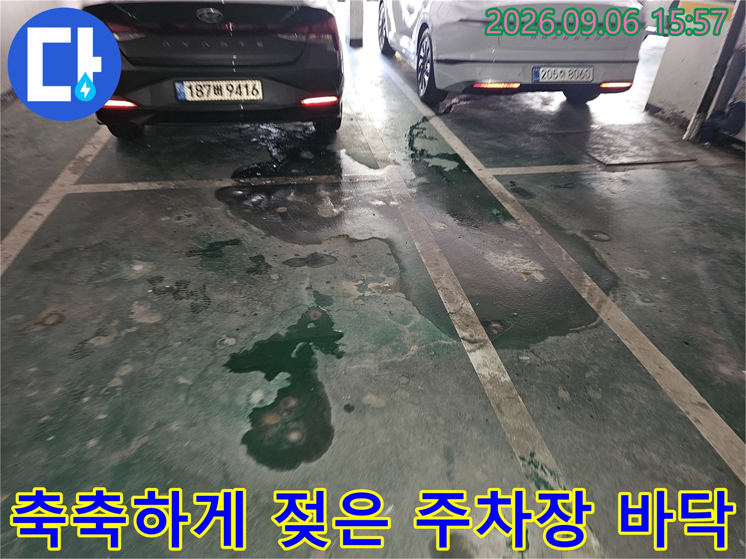 주차 공간 바닥에 물이 고여 있고 어두운 얼룩이 나타난 모습입니다.