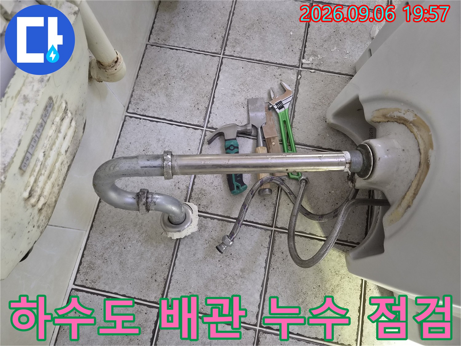 바닥 타일 사이로 연결된 금속 배관과 수리 도구들
