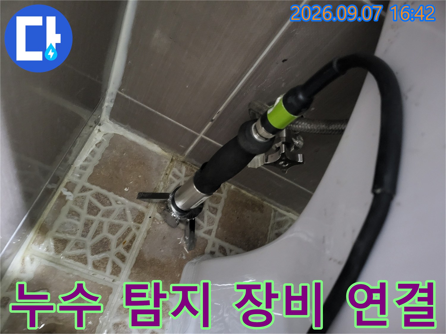 검은색 호스가 연결된 배관 검사용 전문 장비가 화장실 바닥에 위치해 있습니다.