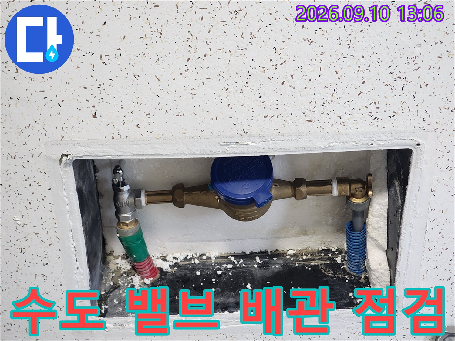 푸른색 수도 밸브와 금속 배관 부속들이 연결된 매립함 내부 사진입니다.