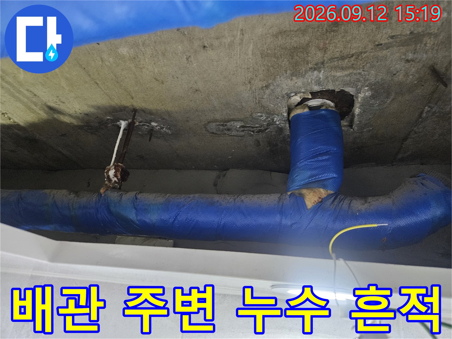 파란색 보온재로 마감된-배관 연결 부위의 습기와 천장 얼룩을 촬영한 사진입니다.