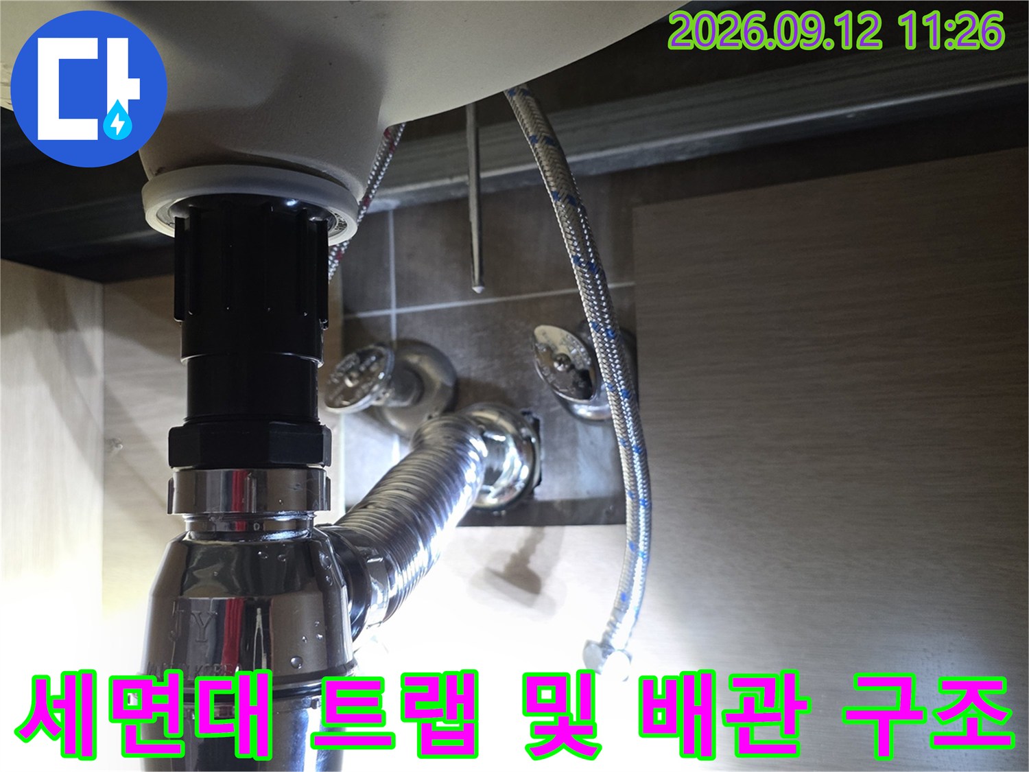 반짝이는 금속 재질의 세면대 배관과 벽면에 연결된 급수 호스 사진입니다.