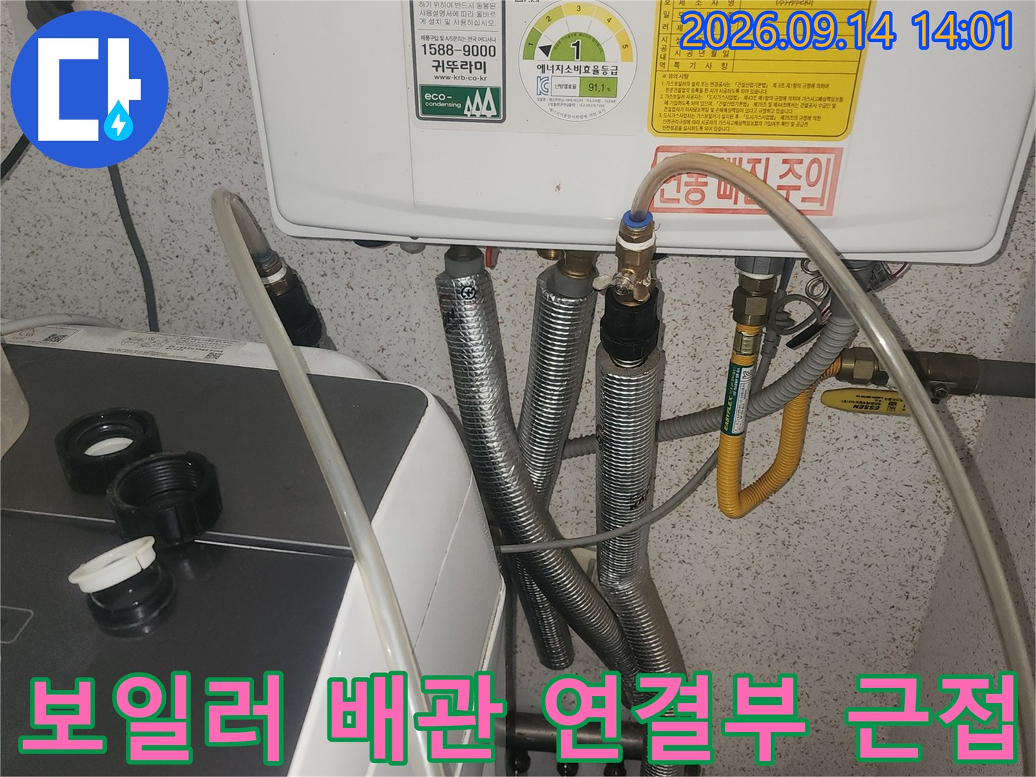보일러 본체 아래로 이어진 금속 주름관과 호스들의 상세 모습