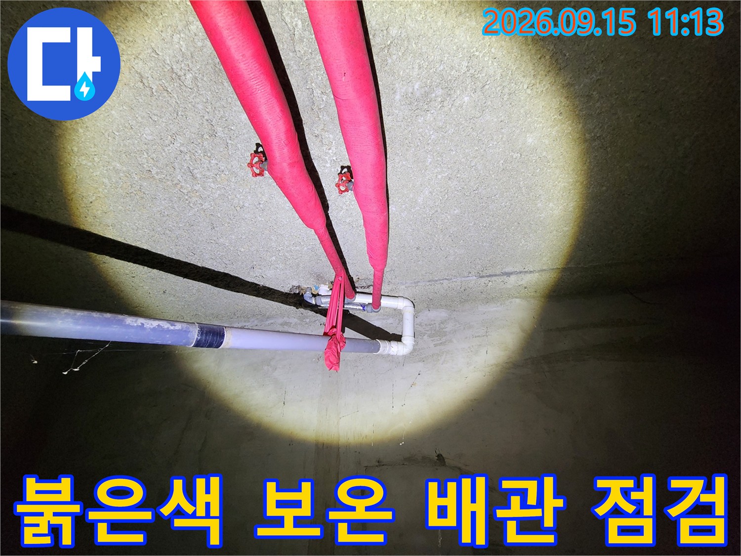 천장에 고정된 붉은색 보온재 배관과 하단 수평 배관의 연결부 모습