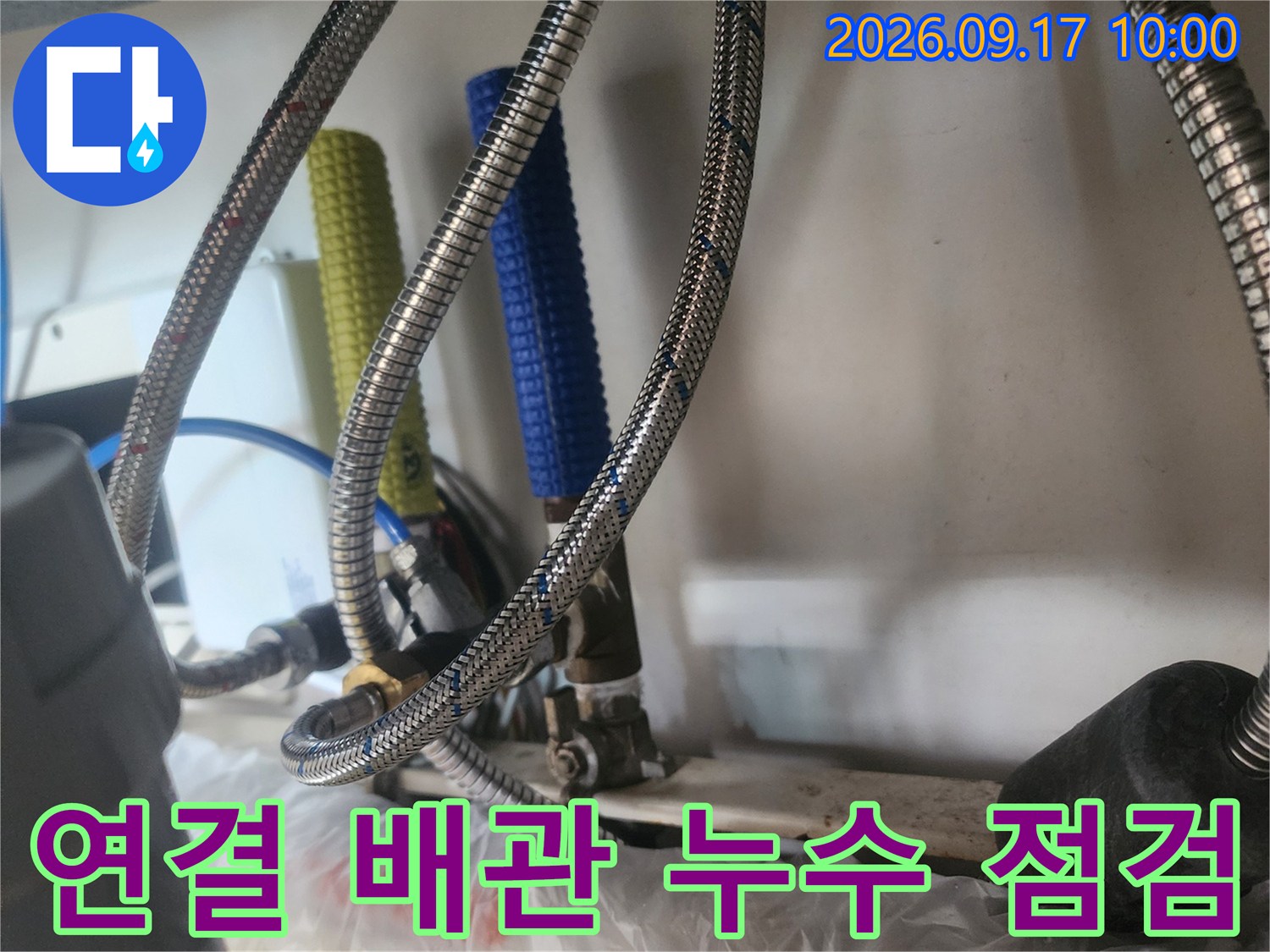 금속 재질의 고압 호스와 보온재가 씌워진 배관이 연결된 싱크대 하단 모습입니다.