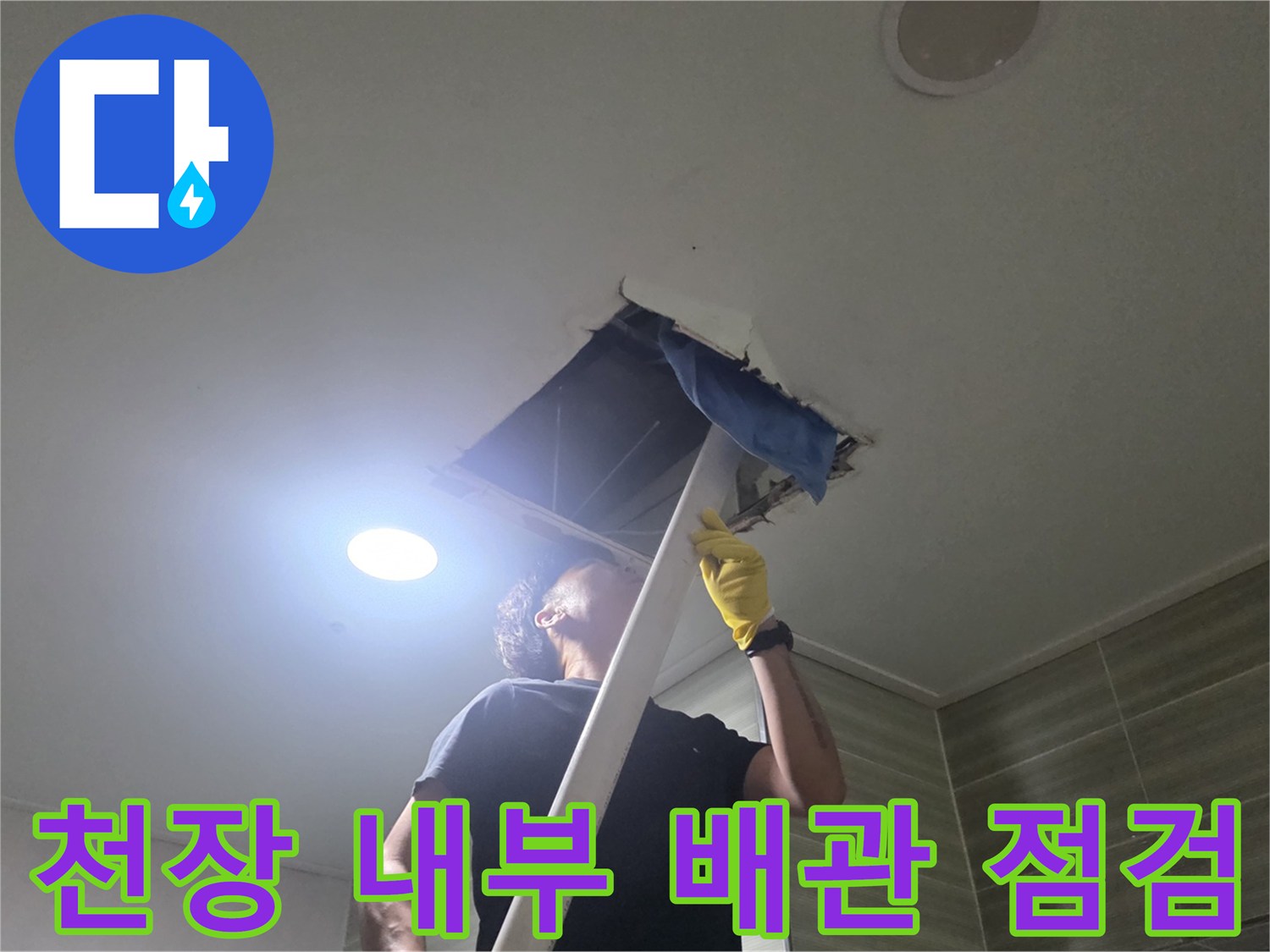 손전등을 이용해 천장 안쪽의 배관 연결 부위를 조사하는 장면